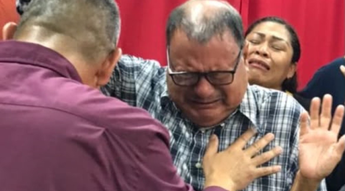Angel Romero praying over a weeping man at the altar